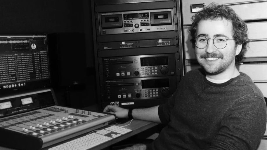 Curtis sitting at a desk in front of a sound board and computer